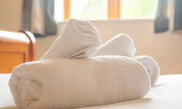 Decorative image of some fluffy white folded towels on a bed suggesting cleanliness and luxury